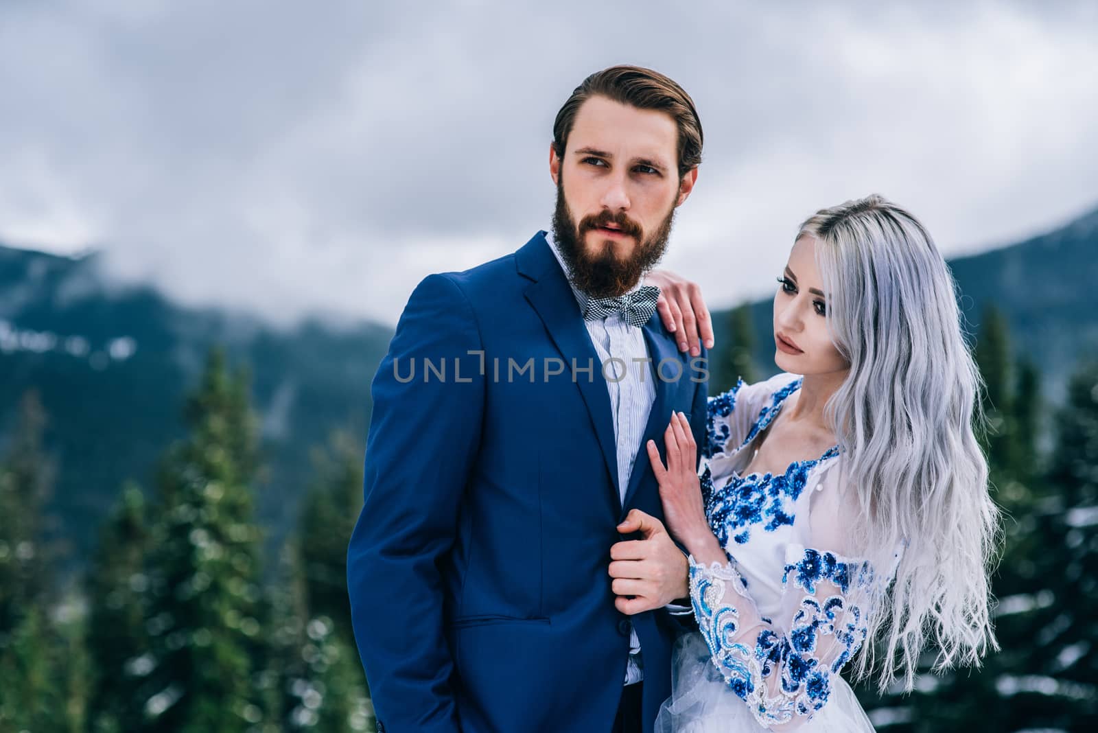 groom in a blue suit and bride in white, embroidered with blue pattern, dress on a background of green pine forests in the mountains of the Carpathians