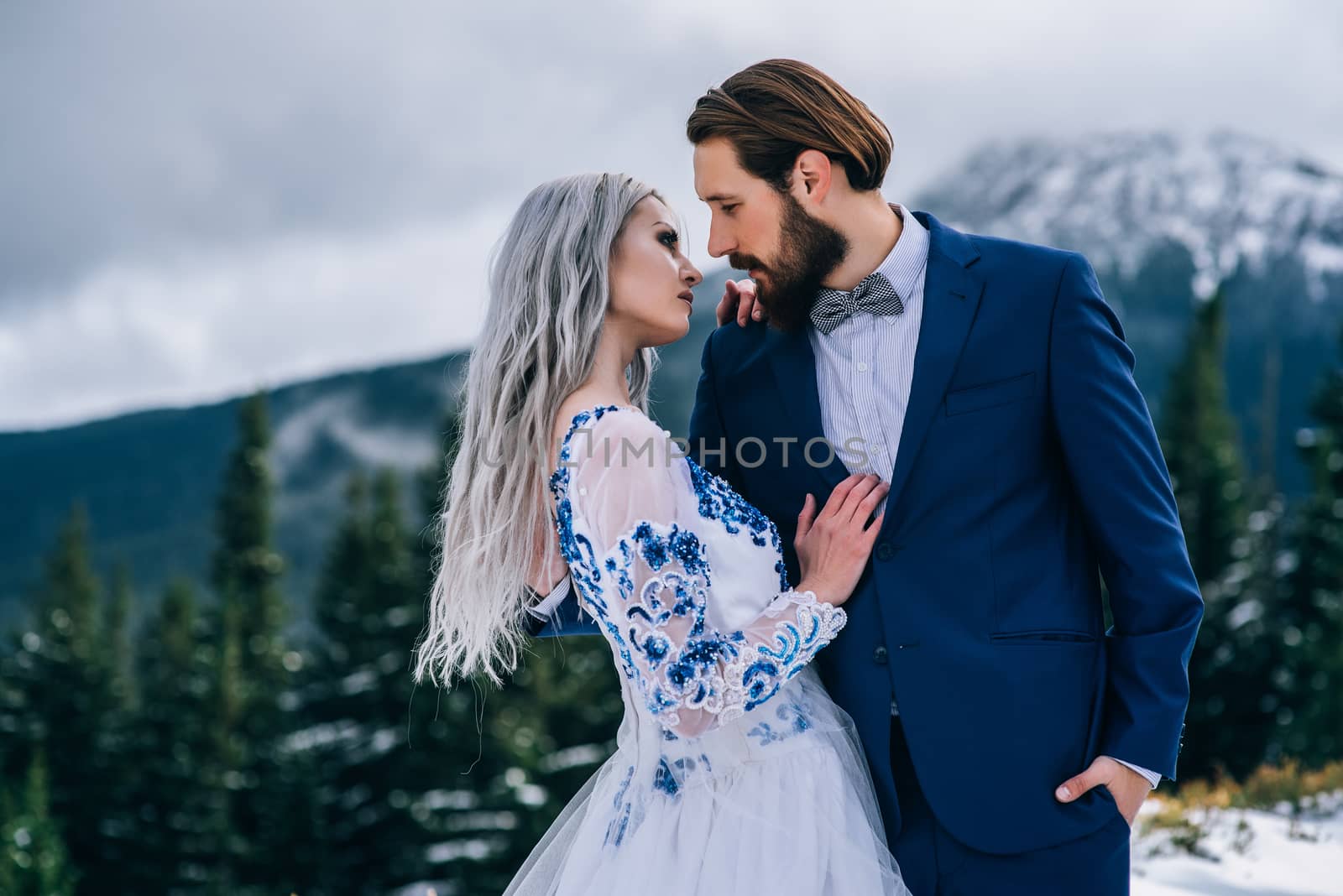 groom in a blue suit and bride in white, embroidered with blue pattern, dress on a background of green pine forests in the mountains of the Carpathians