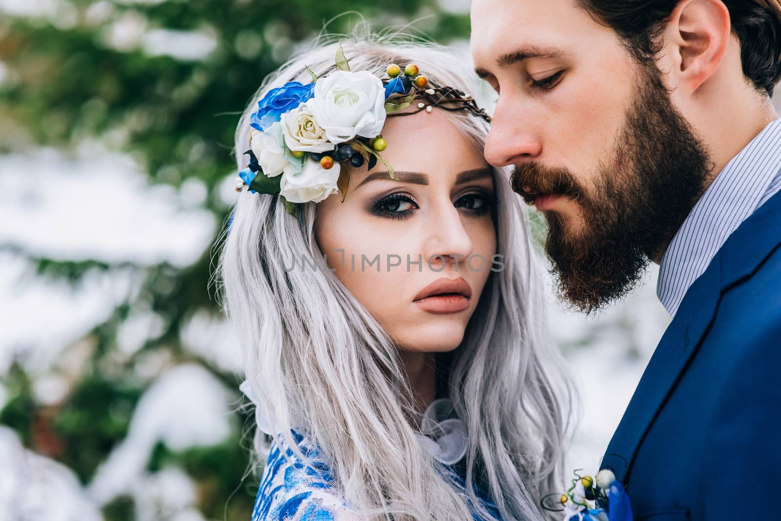 groom in a blue suit and bride in white, embroidered with blue pattern, dress on a background of green pine forests in the mountains of the Carpathians