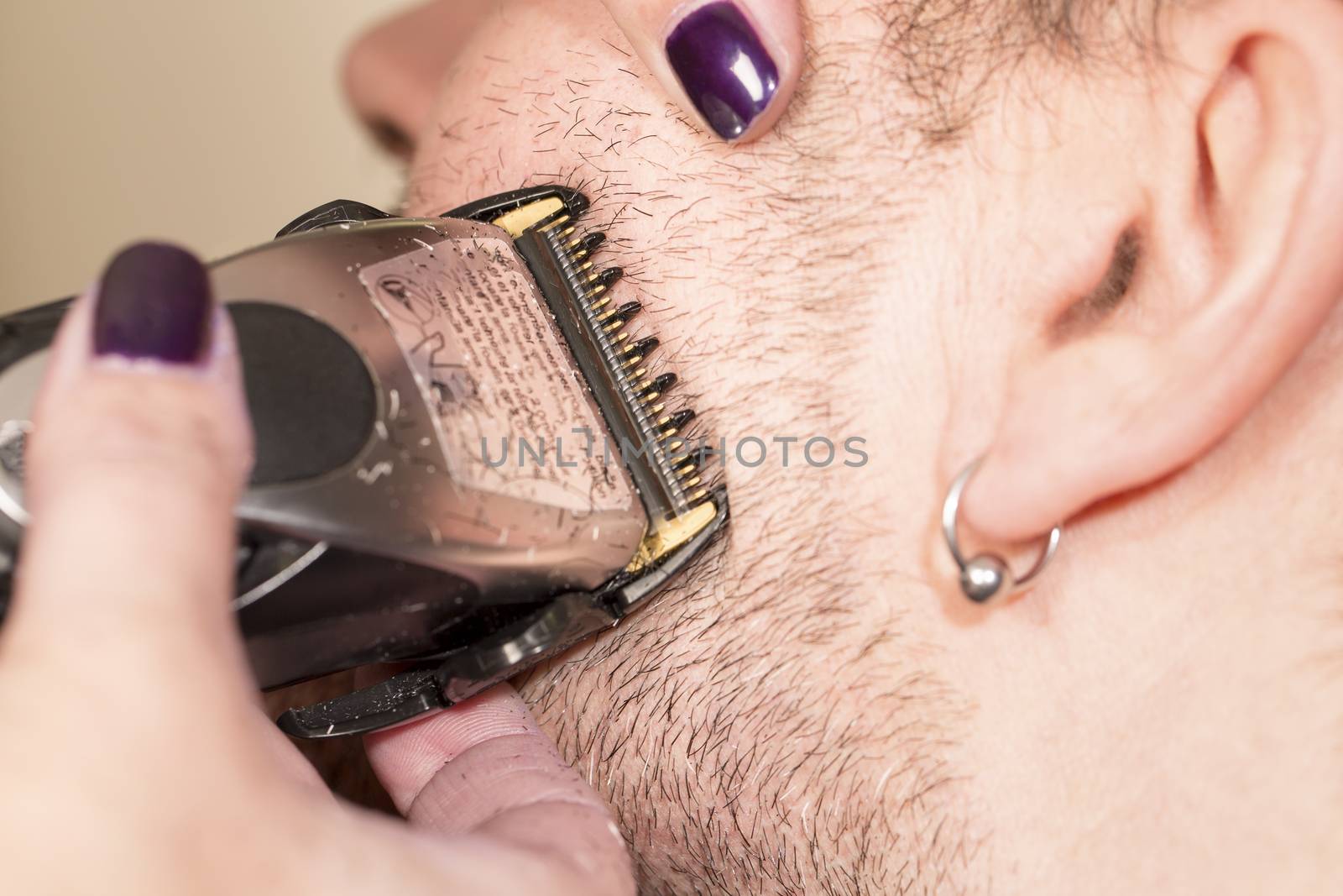 Hairdresser, cutting beard of his customer with scissors and shave in the salon