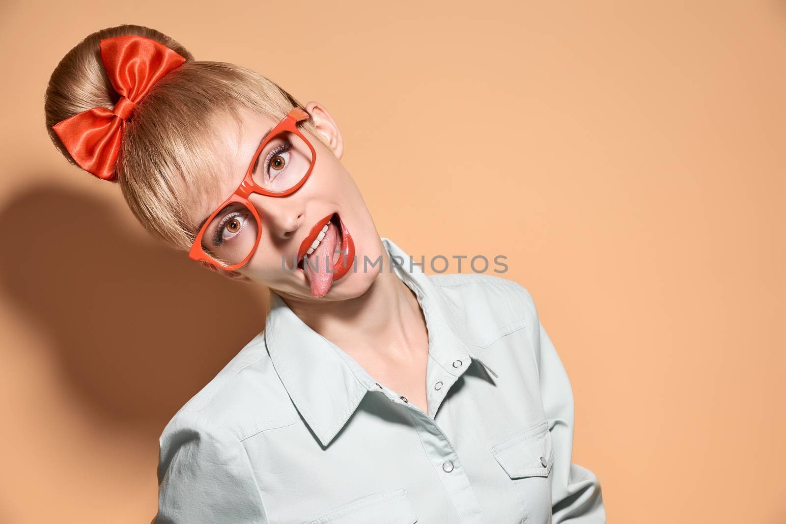 Beauty fashion portrait woman in stylish glasses, tongue hanging out. Attractive pretty blonde sexy hipster girl. Confidence, success, Pinup hairstyle, red bow. Unusual playful, creative. Vintage