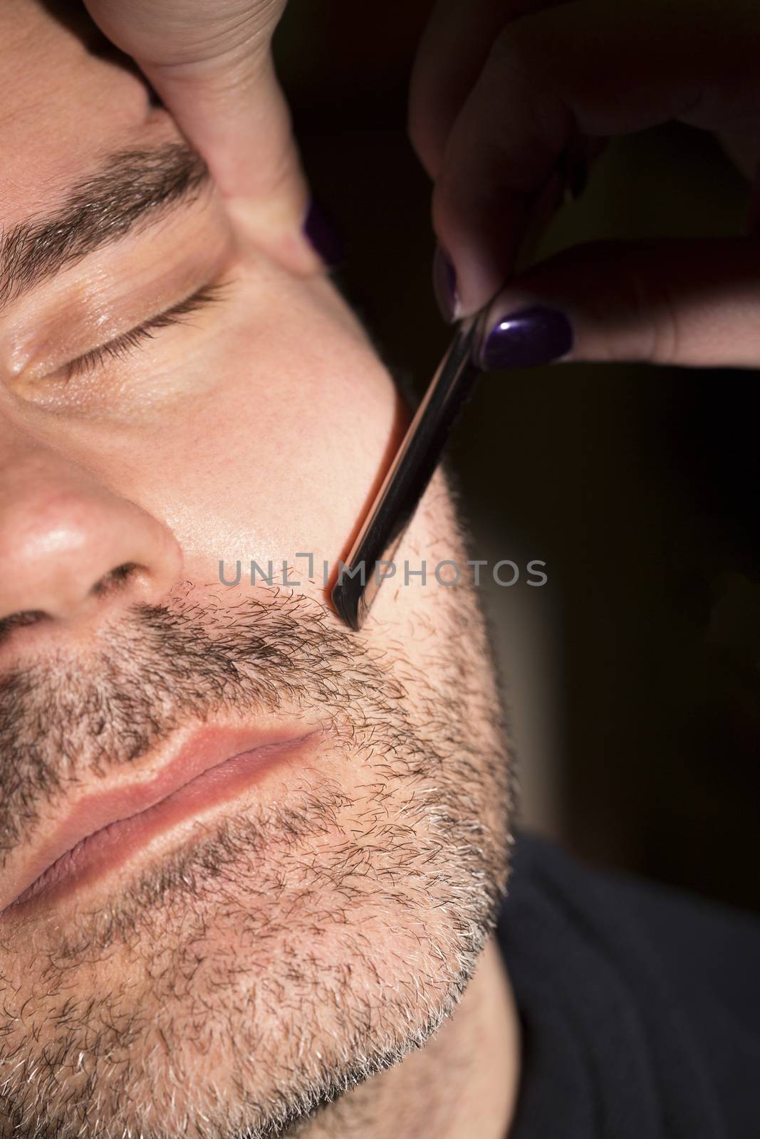 Hairdresser, cutting beard of his customer with scissors and shave in the salon