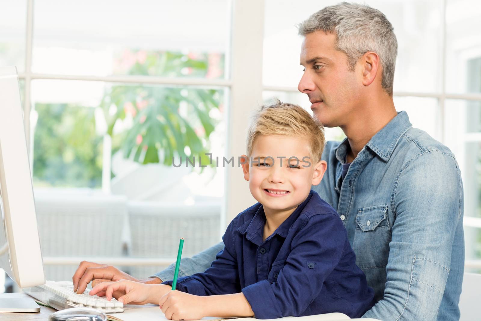 Father and son at the desk using computer and drawing