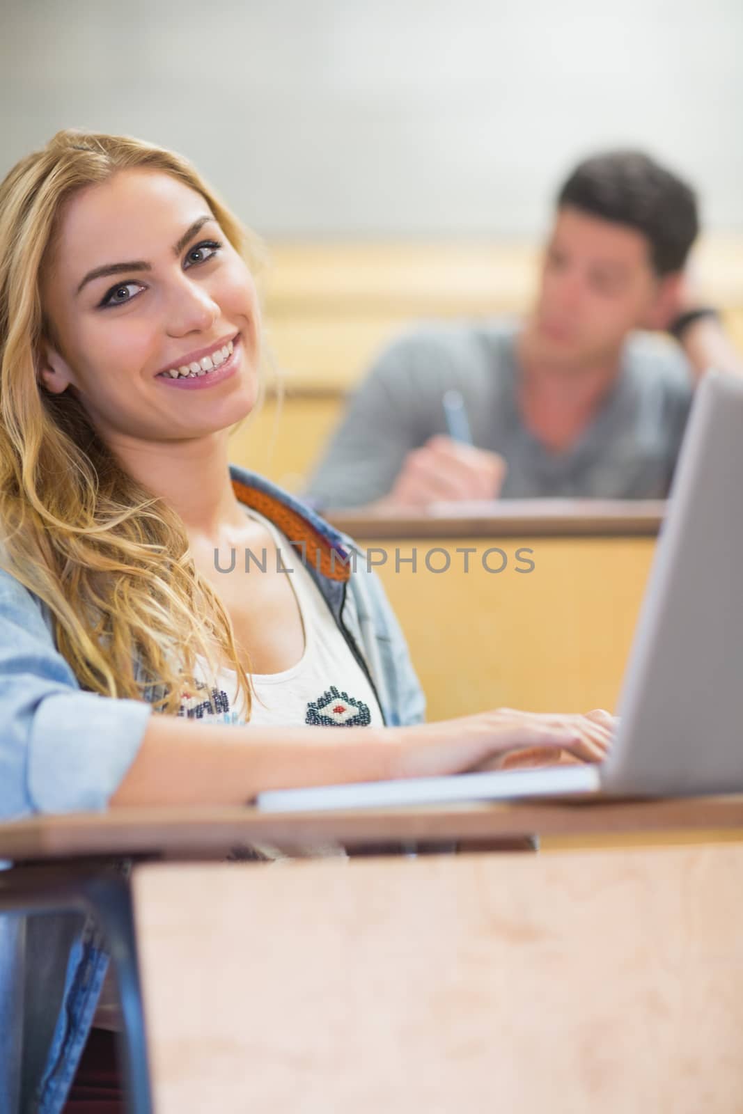 Smiling attractive student using laptop at the lecture hall