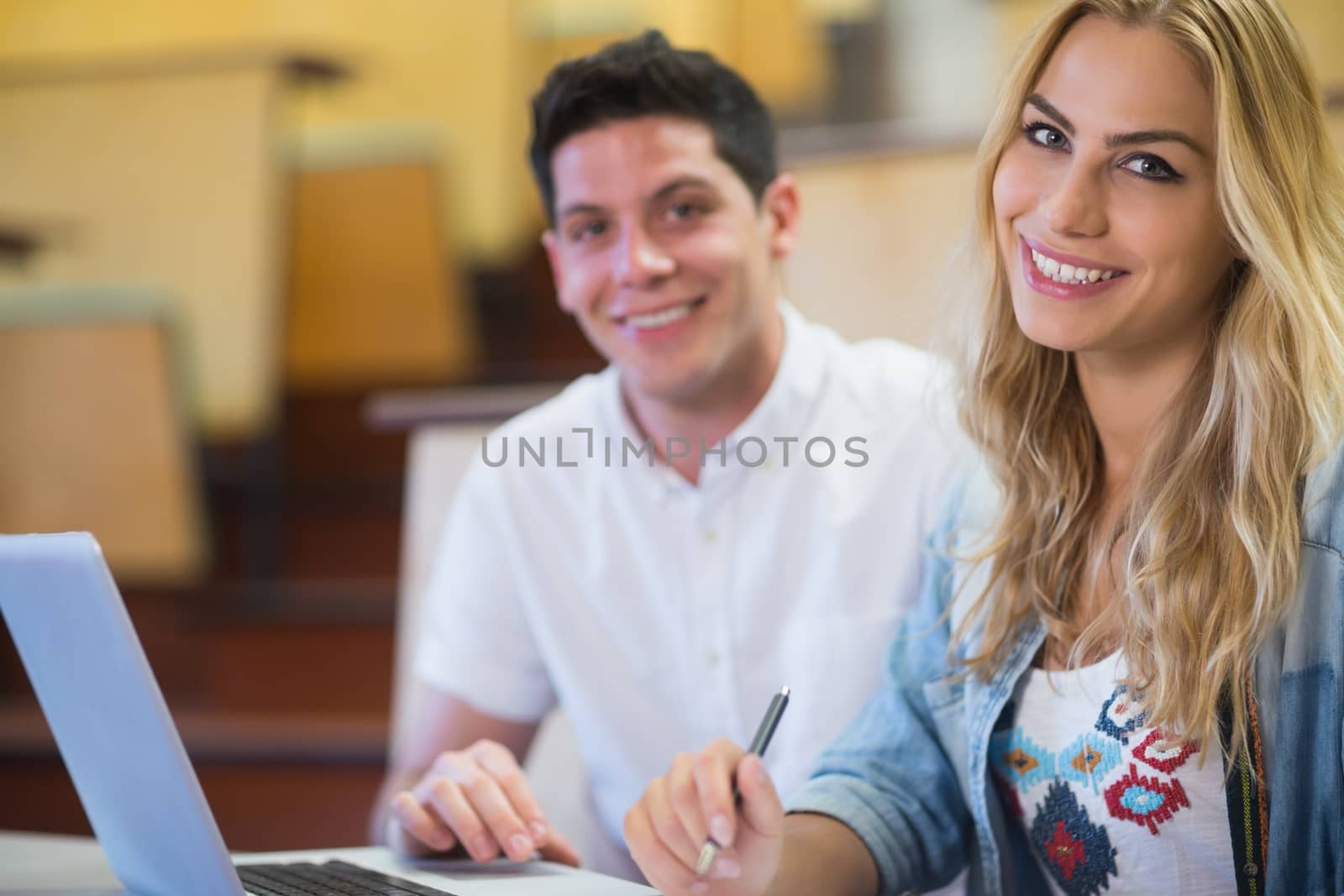 Smiling college students using laptop at the amphitheater