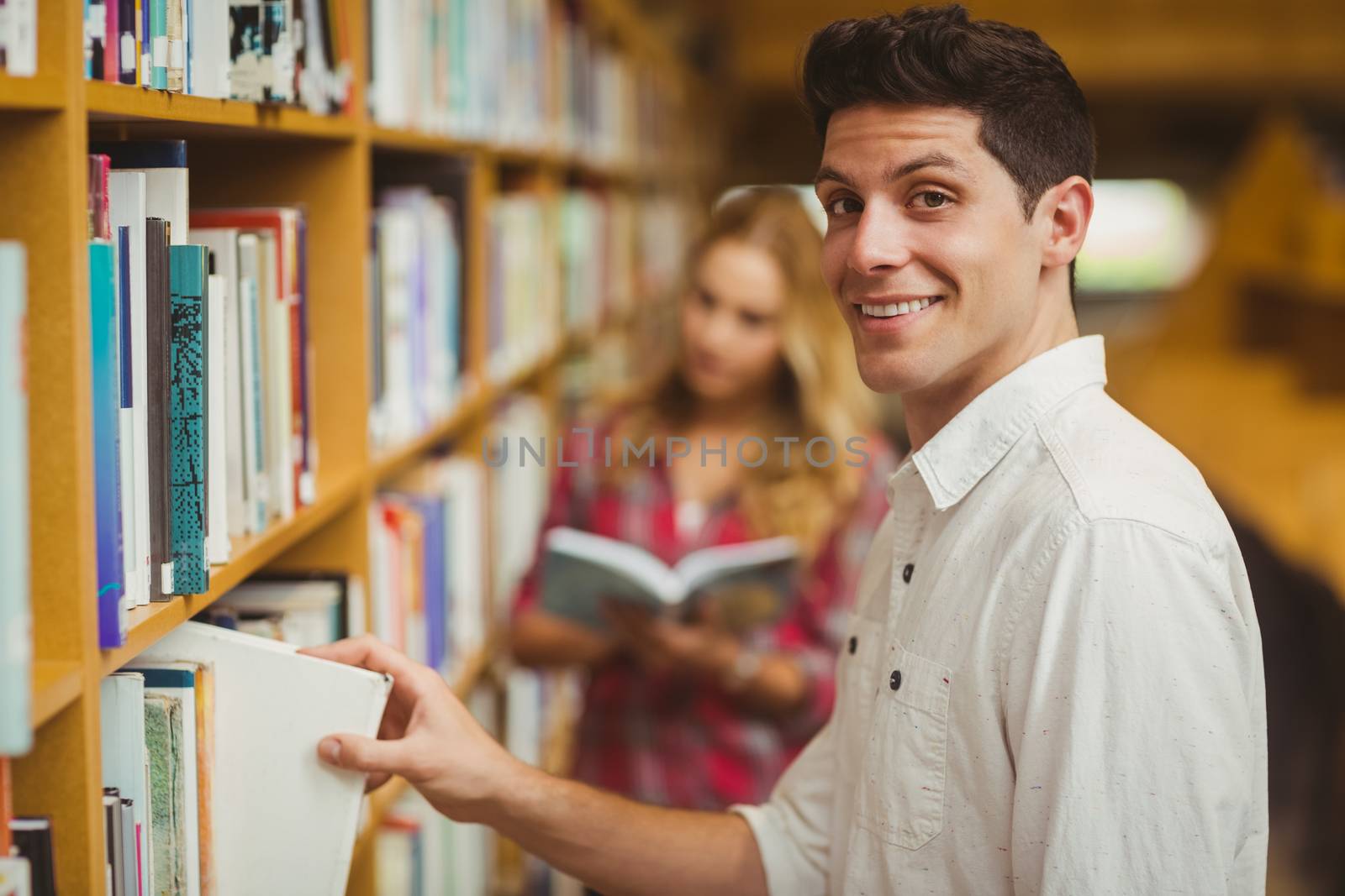 Smiling male student taking book in library
