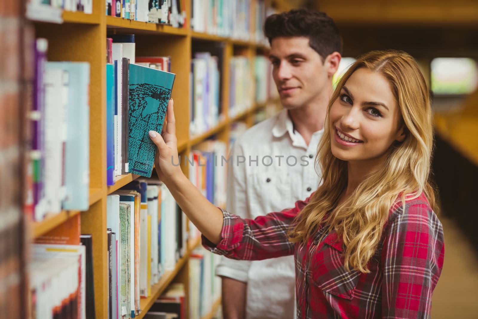 Smiling female student taking book in library