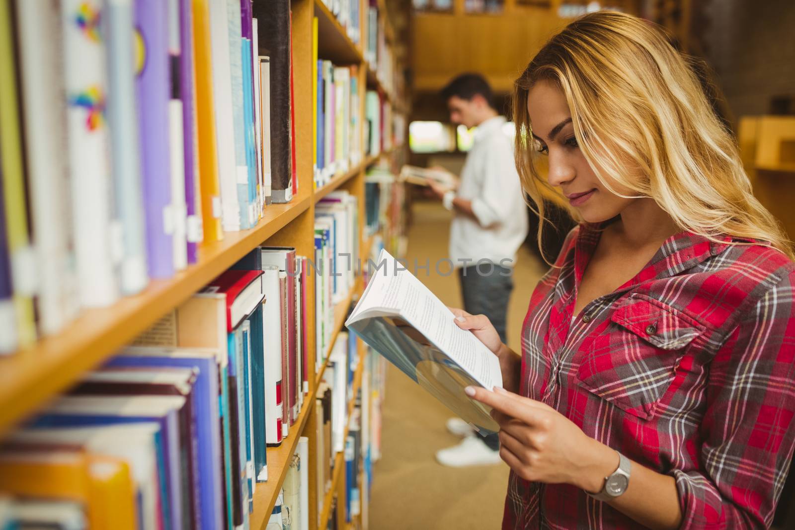 Attractive female student reading book in library