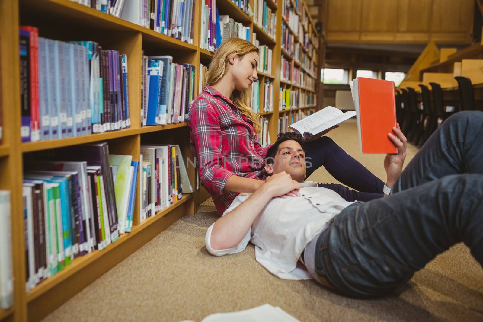 Student reading book while lying on his classmate in library