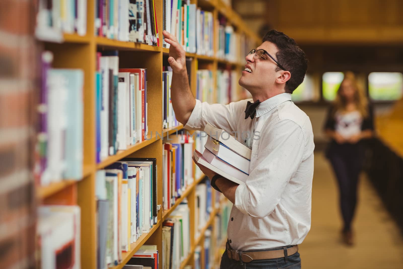 Nerd searching book while girl walking to him in library