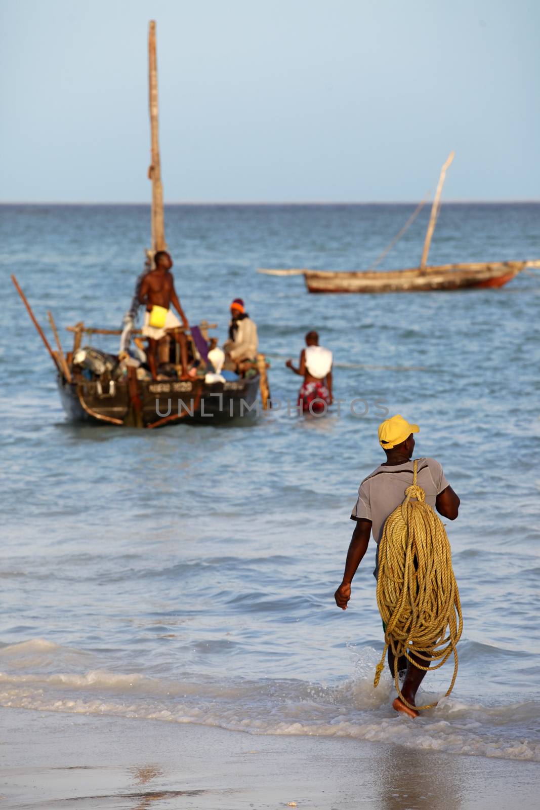 Stone Town (Zanzibar), Tanzania - January 6, 2016: A dhow (traditional sailboat) in the background and a crowded fishing boat and fishman in the foreground in the Indian Ocean just off the island of Zanzibar, Nungwi