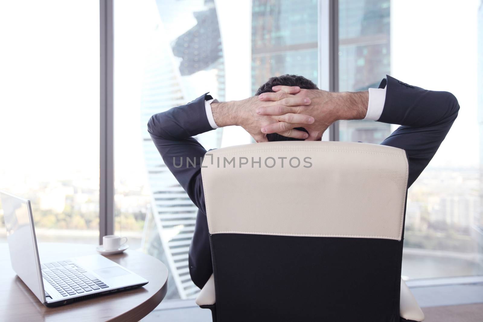 Businessman relaxes sitting in the office and looking in window