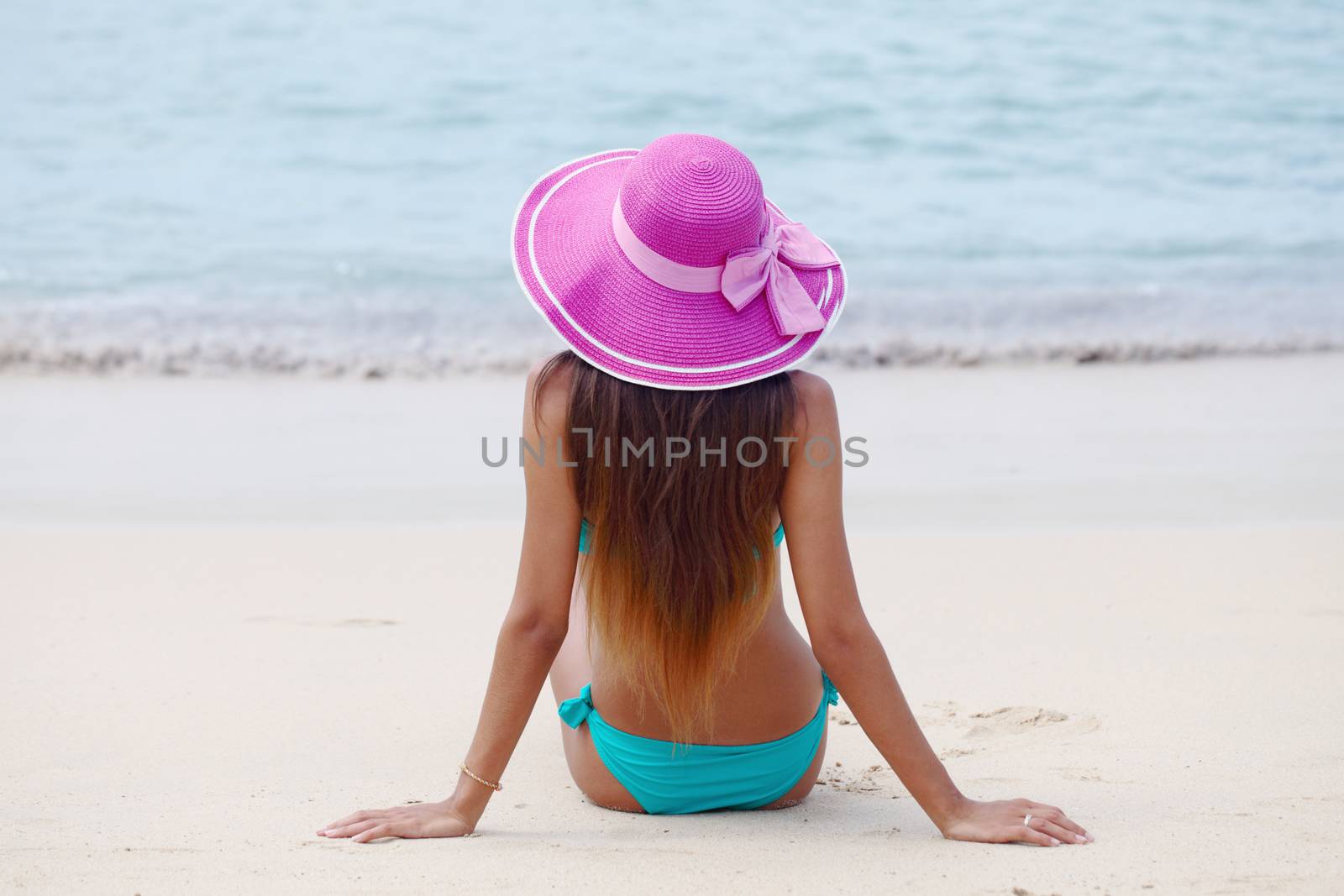 Woman in big hat sitting on beach by the sea