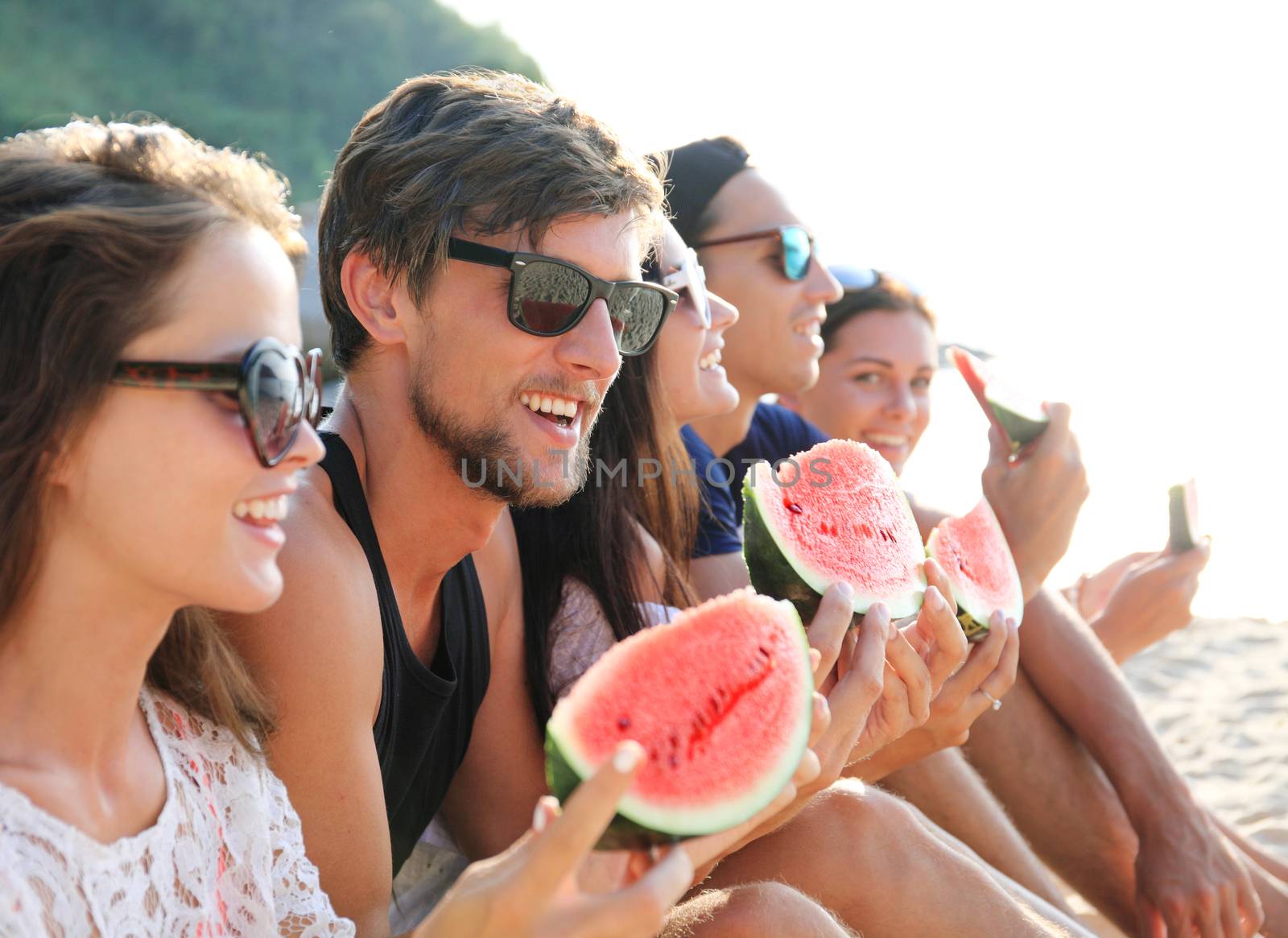 Friends eating watermelon on beach by ALotOfPeople