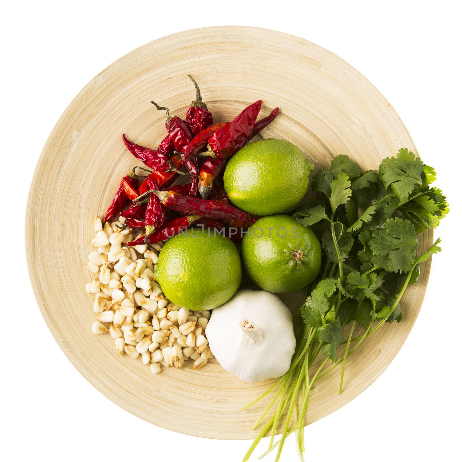 Dried hominy, garlic, lime, cilantro and hot peppers: ingredients for a version of a posole.  On wooden plate and isolated on a white background.