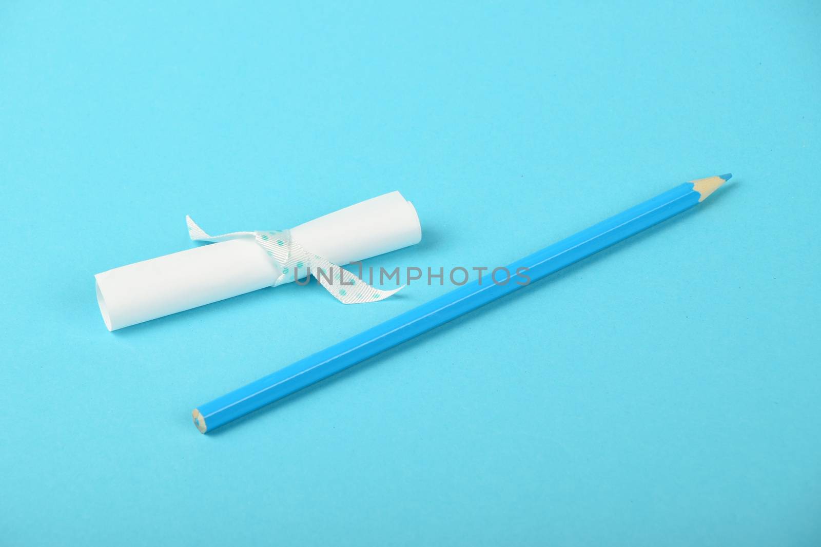 White small paper scroll note with ribbon and pencil on tender blue background