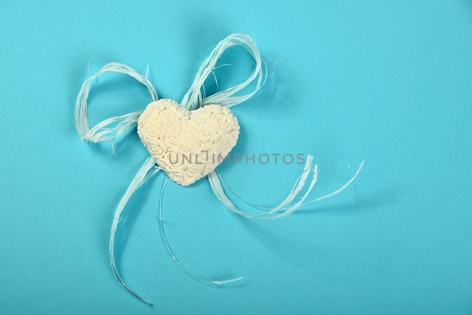 One gypsum alabaster handmade toy heart with roses flowers relief and rope on tender blue design paper background