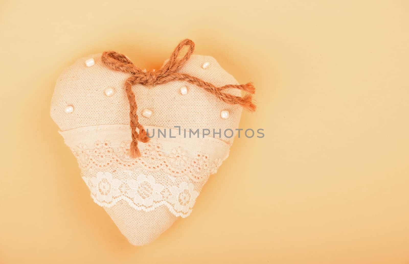 Valentine template, handmade beige toy textile lace heart with burlap jute bow, beads and copy space on paper background