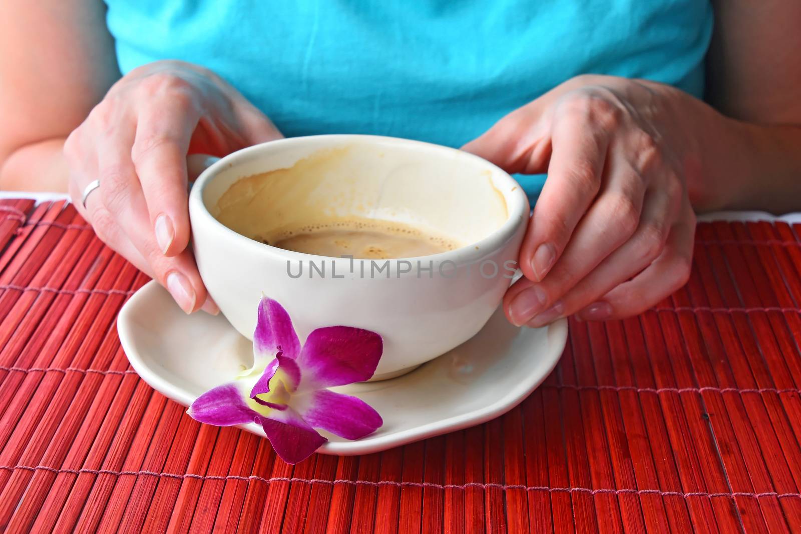 Woman two hands holding half empty latte coffee cup with orchid flower at porcelain saucer