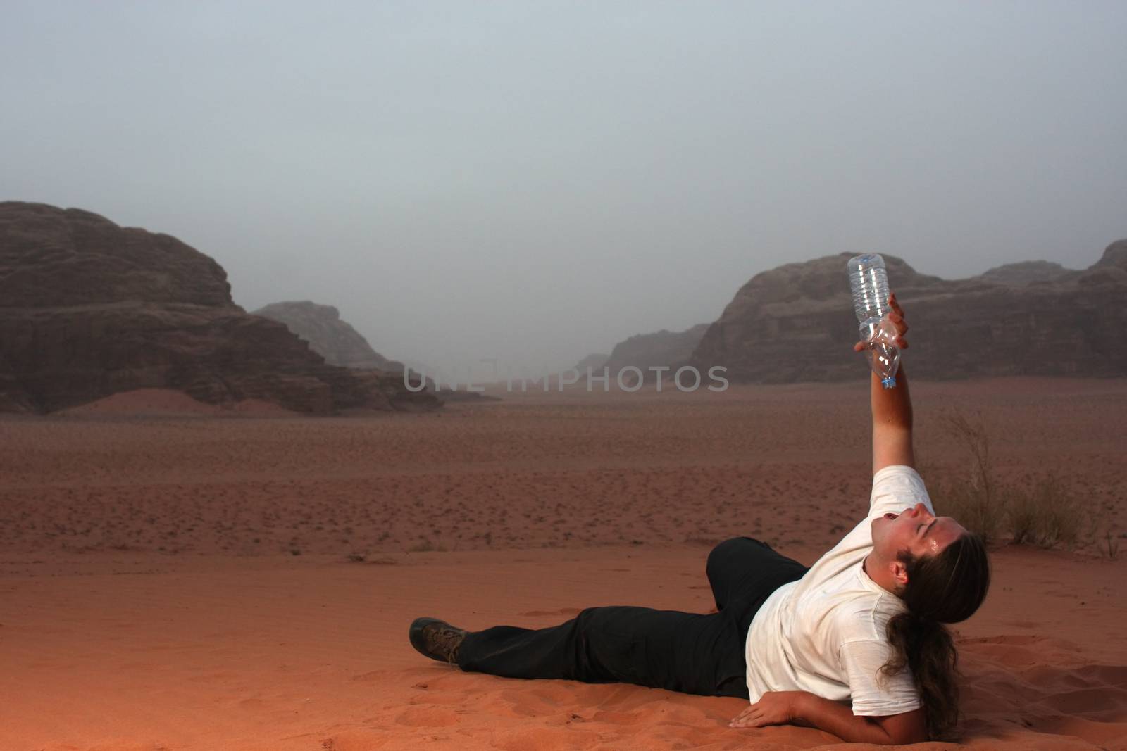 Desperate man in the desert drinking last drops of water from an empty bottle