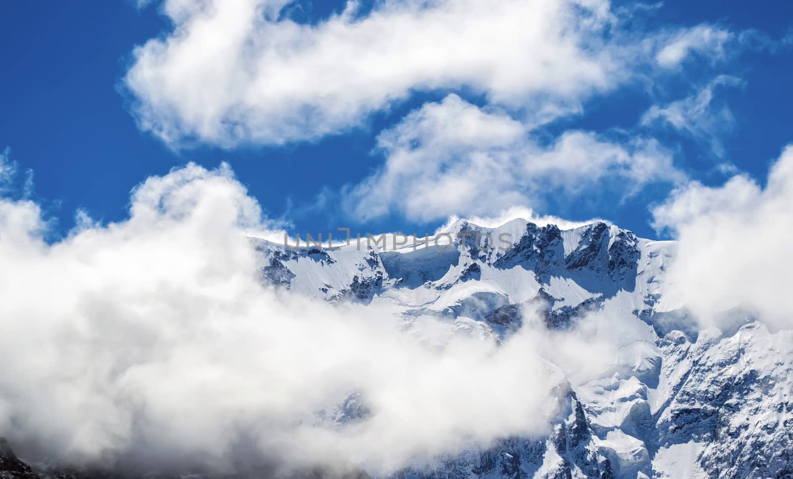 Close view of snowy mountain ridge shrouded in clouds. Blue sky. Clear summit. North Caucasus.