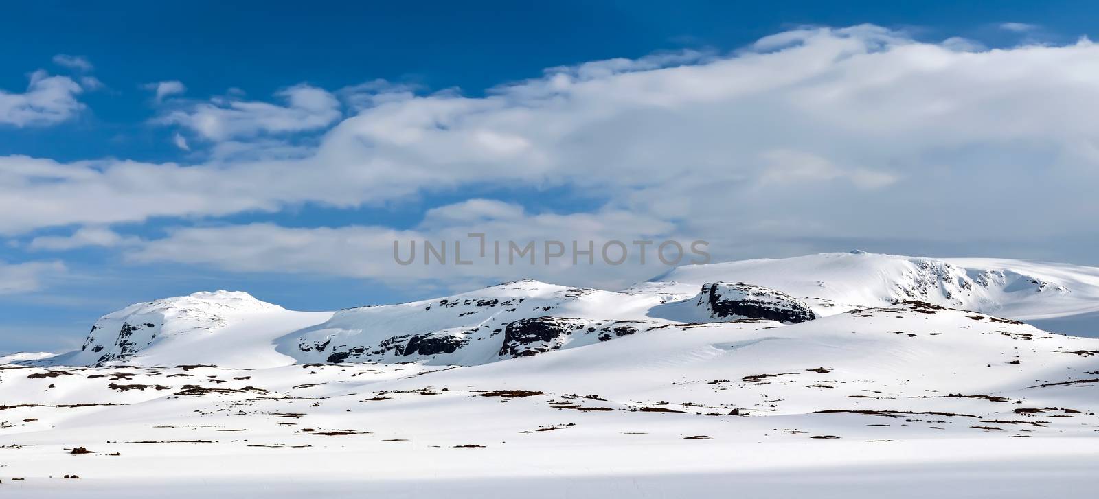 Snowy mountain range in the sunlight. Clouds, blue sky. Winter.  Finse, Norway.