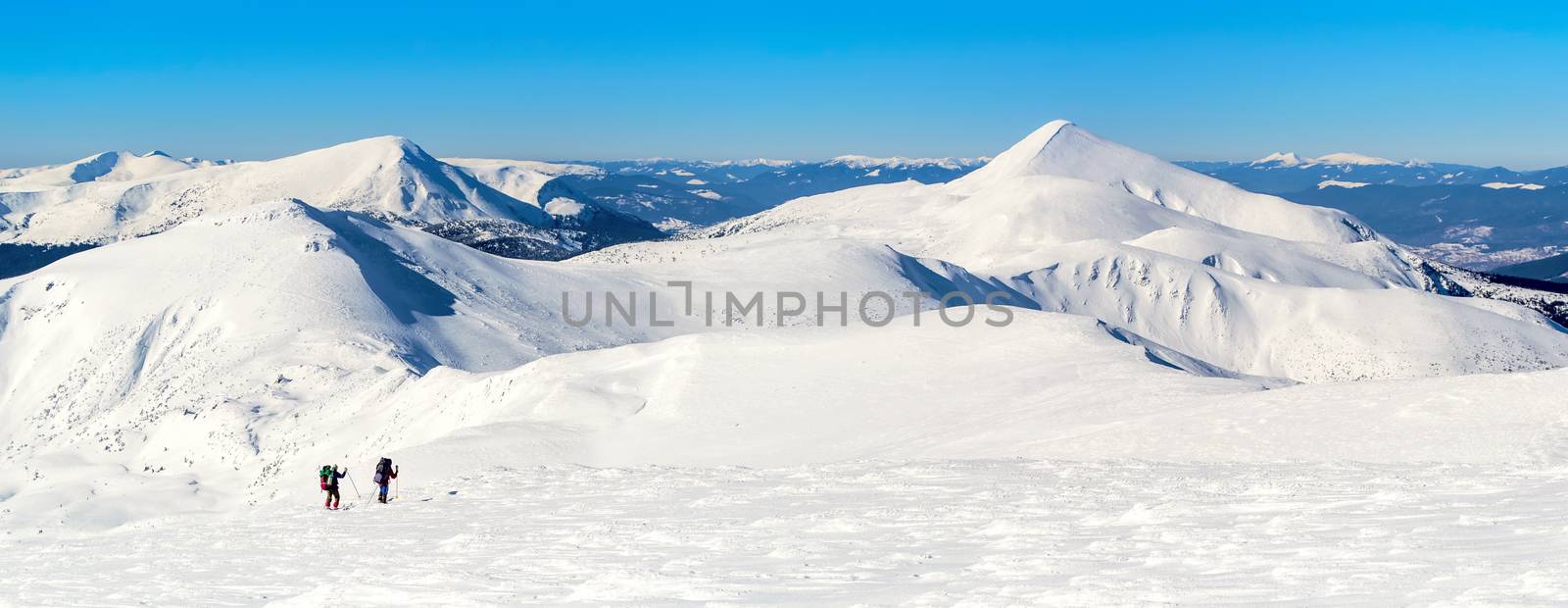Ski touring on snowy mountain ridge. Two men with backpacks. The sky is clear, sunny. Winter. Ukraine