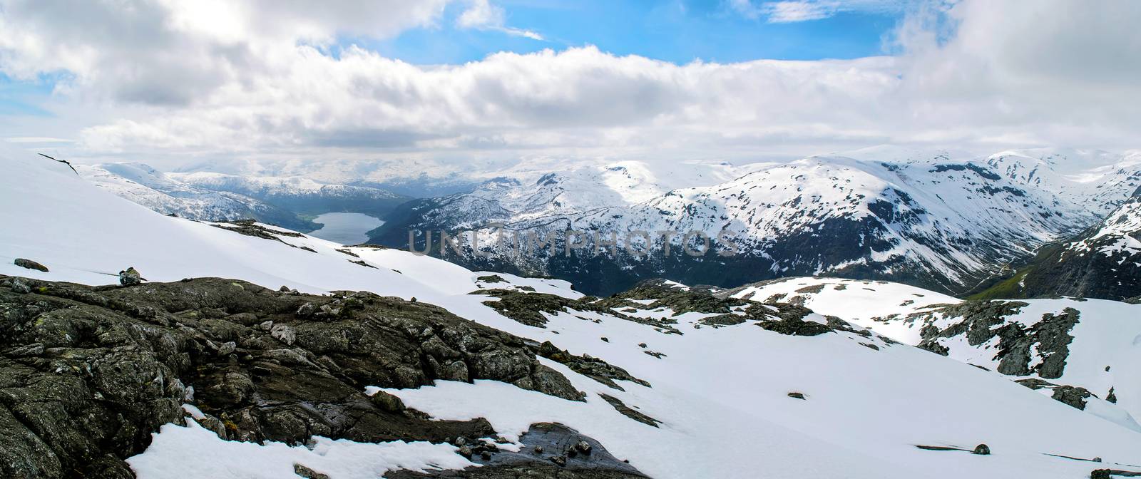 Scenic view on snowy mountains of Norway. Cliffs stones, snow, lake.