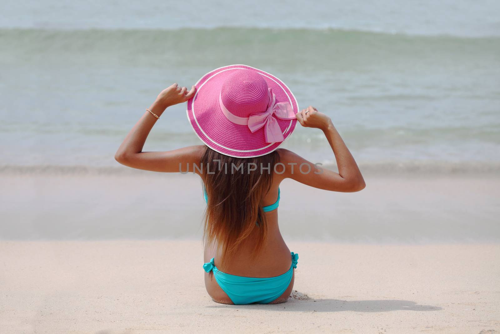 Woman in big hat sitting on beach by the sea