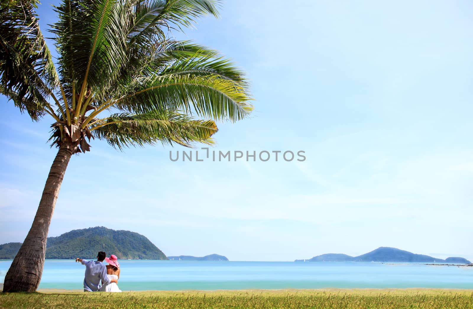 Happy young caucasian couple sitting under palm near the sea 