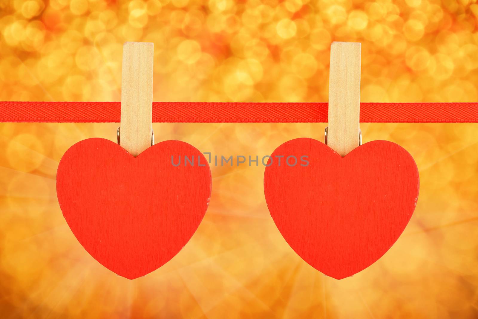 Valentine day template, two red wooden hearts with clothes pins on textile ribbon over golden festive glitter blur