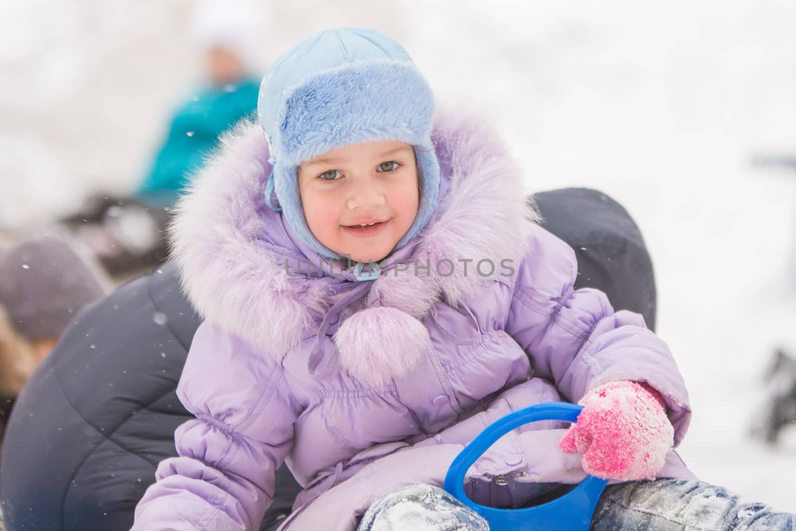 Five-year girl riding winter on a snowy hill surrounded by other children