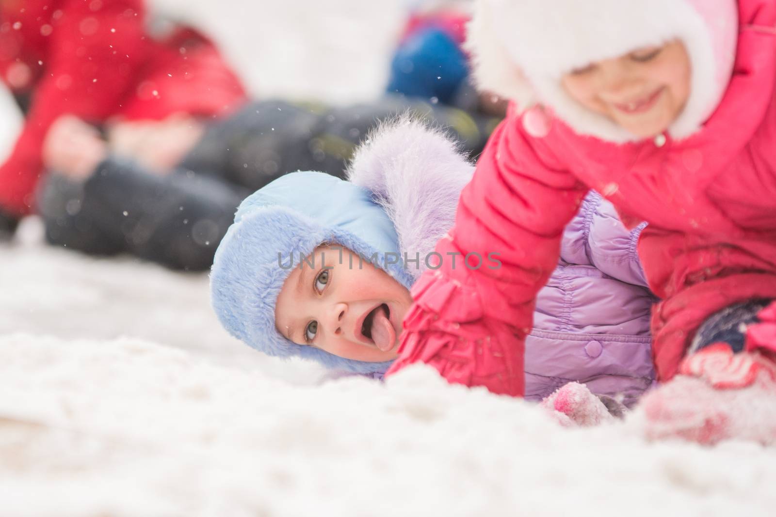Two girls in the winter ride on a snowy hill surrounded by other children