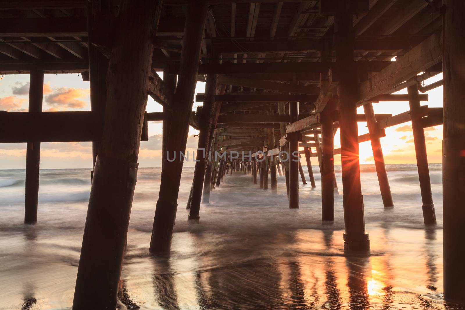 Under the San Clemente pier on the beach at sunset in the fall in Southern California, United States.