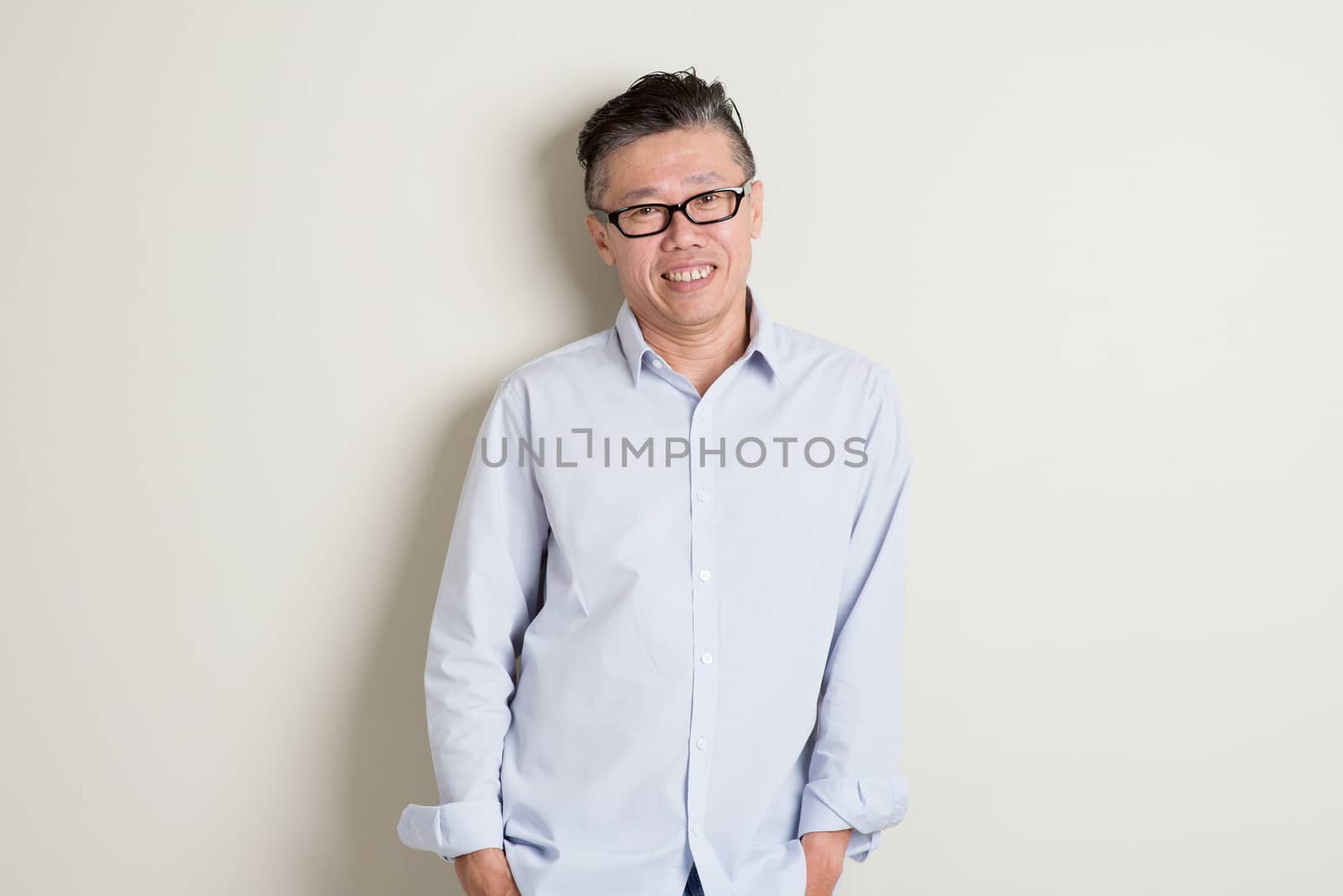 Portrait of happy single mature 50s Asian man in casual business smiling, standing over plain background with shadow.