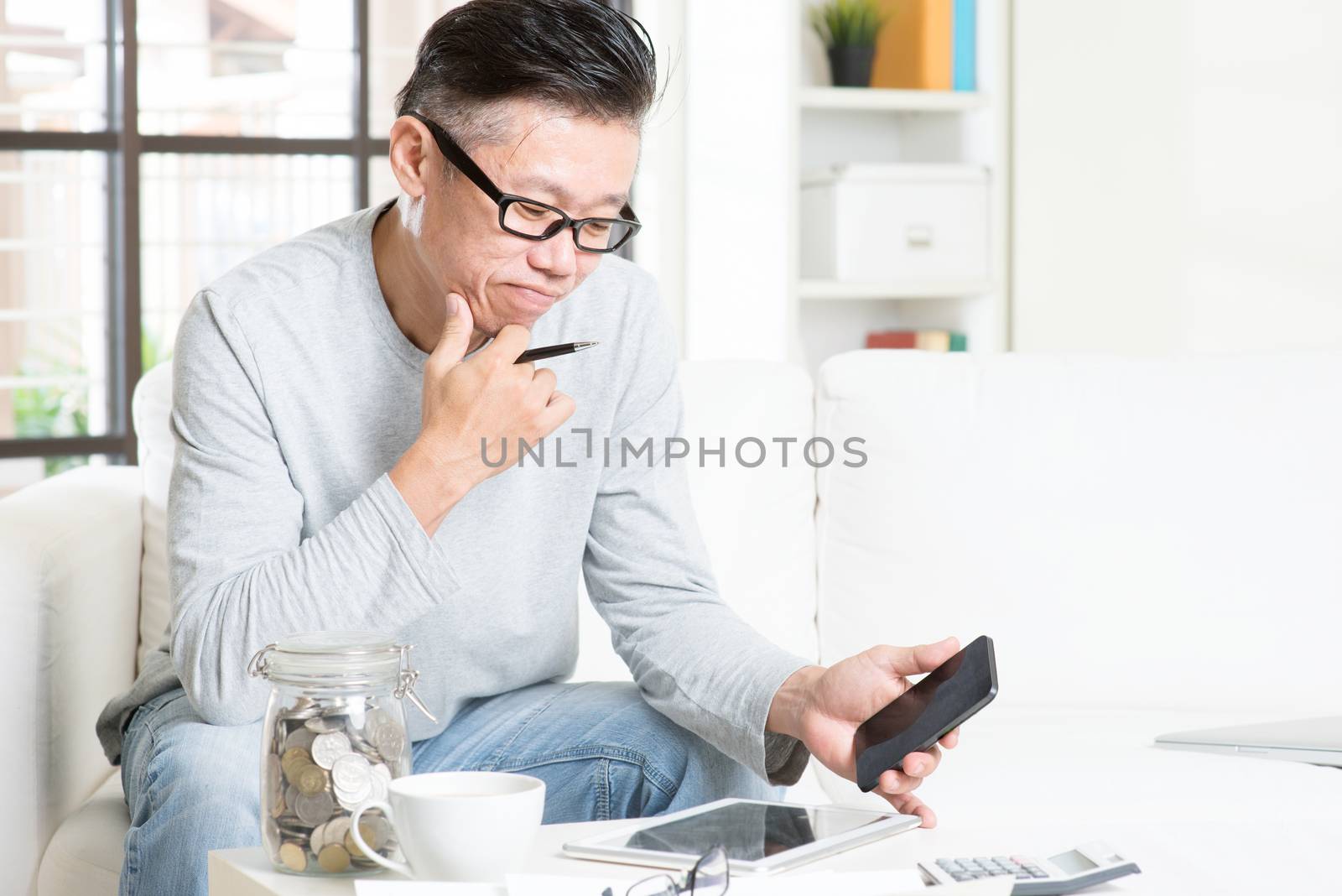 Mature 50s Asian man doing analysis on his business budget, looking on tablet pc and smart phone. Saving, retirement, retirees financial planning concept.