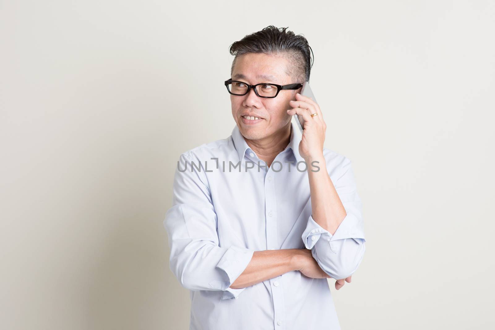 Portrait of single mature 50s Asian man in casual business calling on  smartphone and smiling, standing over plain background with shadow. Chinese senior male people.