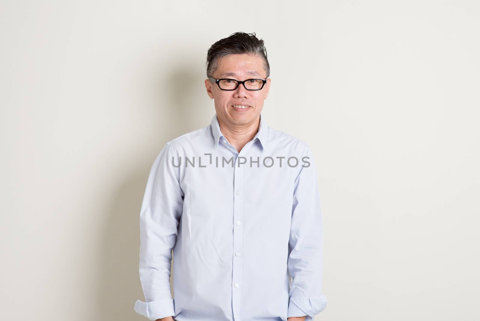 Portrait of confident single mature 50s Asian man in casual business smiling, standing over plain background with shadow.