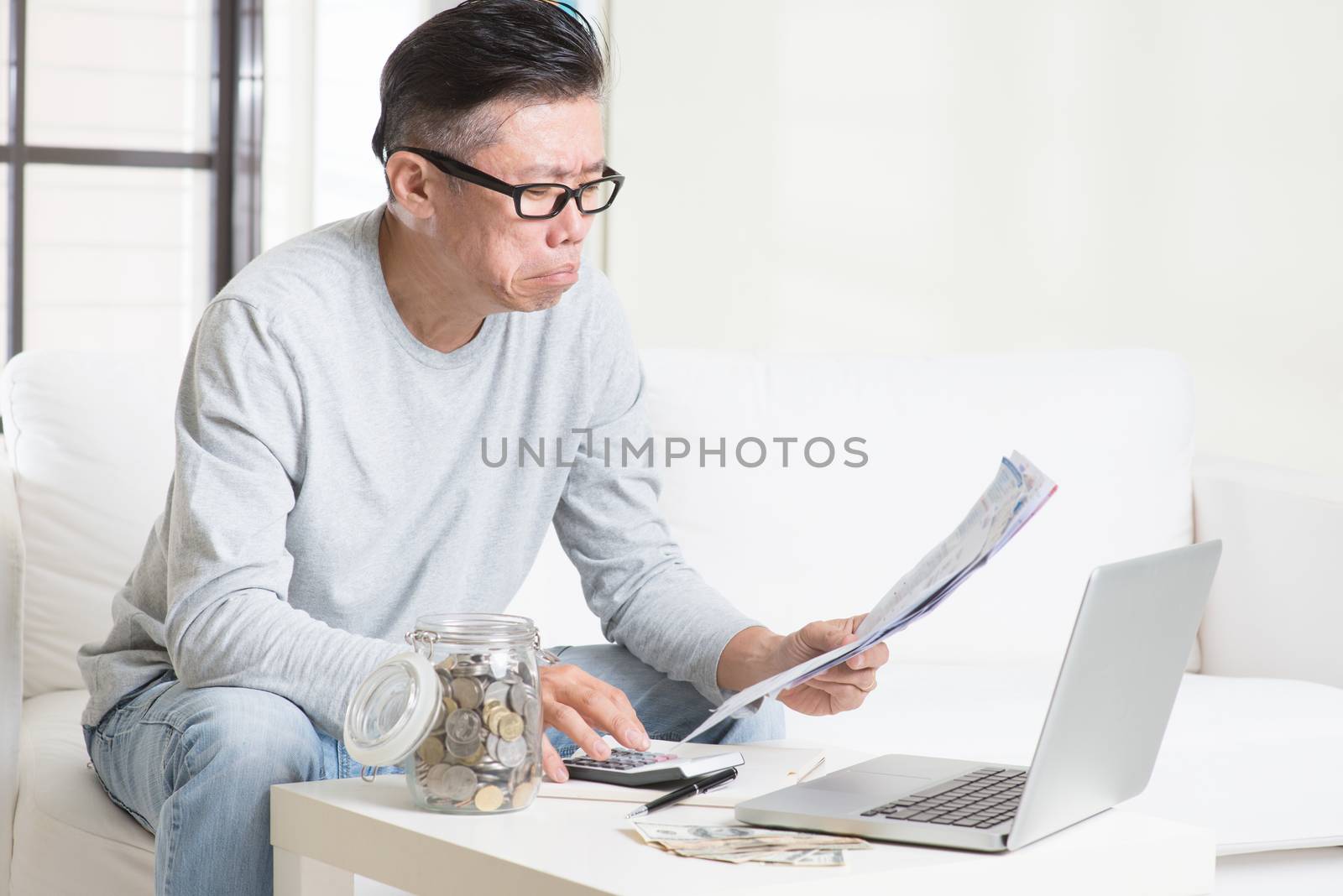 Worried mature Asian man looking at the bills. by szefei