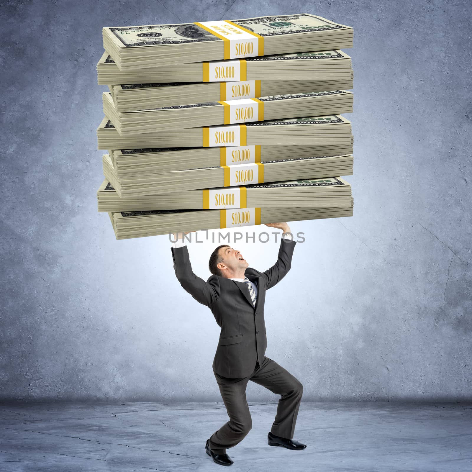 Businessman holding heavy big stack of money on grey wall background