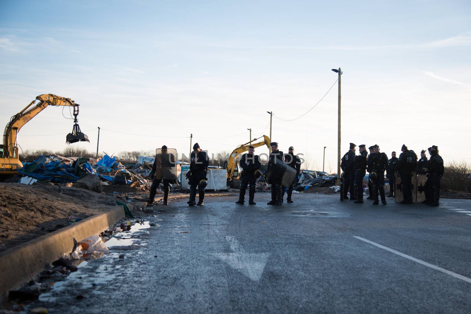 FRANCE, Calais: Policemen stand as bulldozers demolish part of the Jungle in Calais, northern France on January 25, 2016.