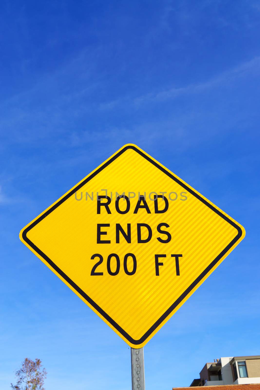 Yellow road ends ahead in 200 feet road sign with black lettering against blue sky.