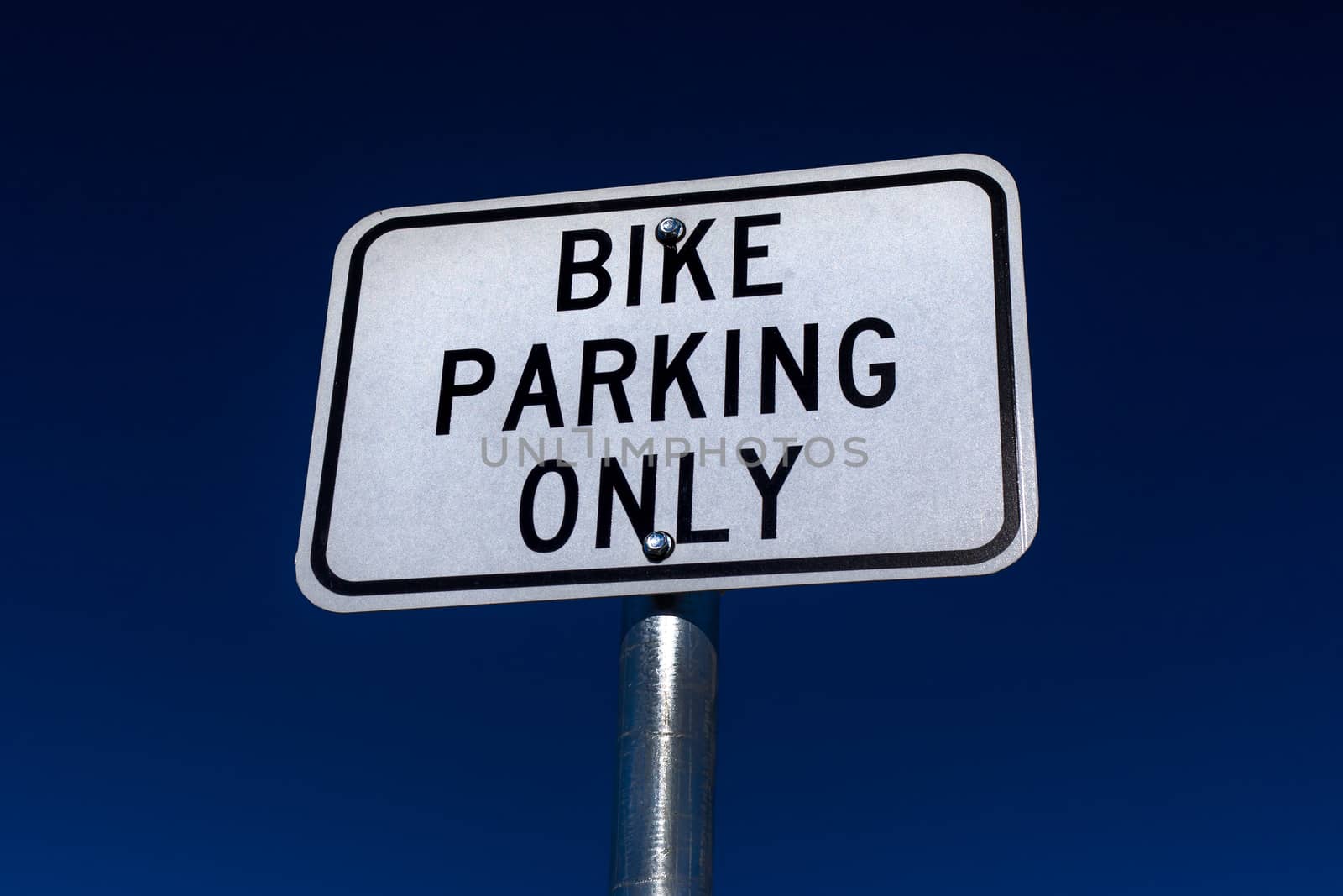 Bicycle parking only sign with black letters on white background and blue sky.