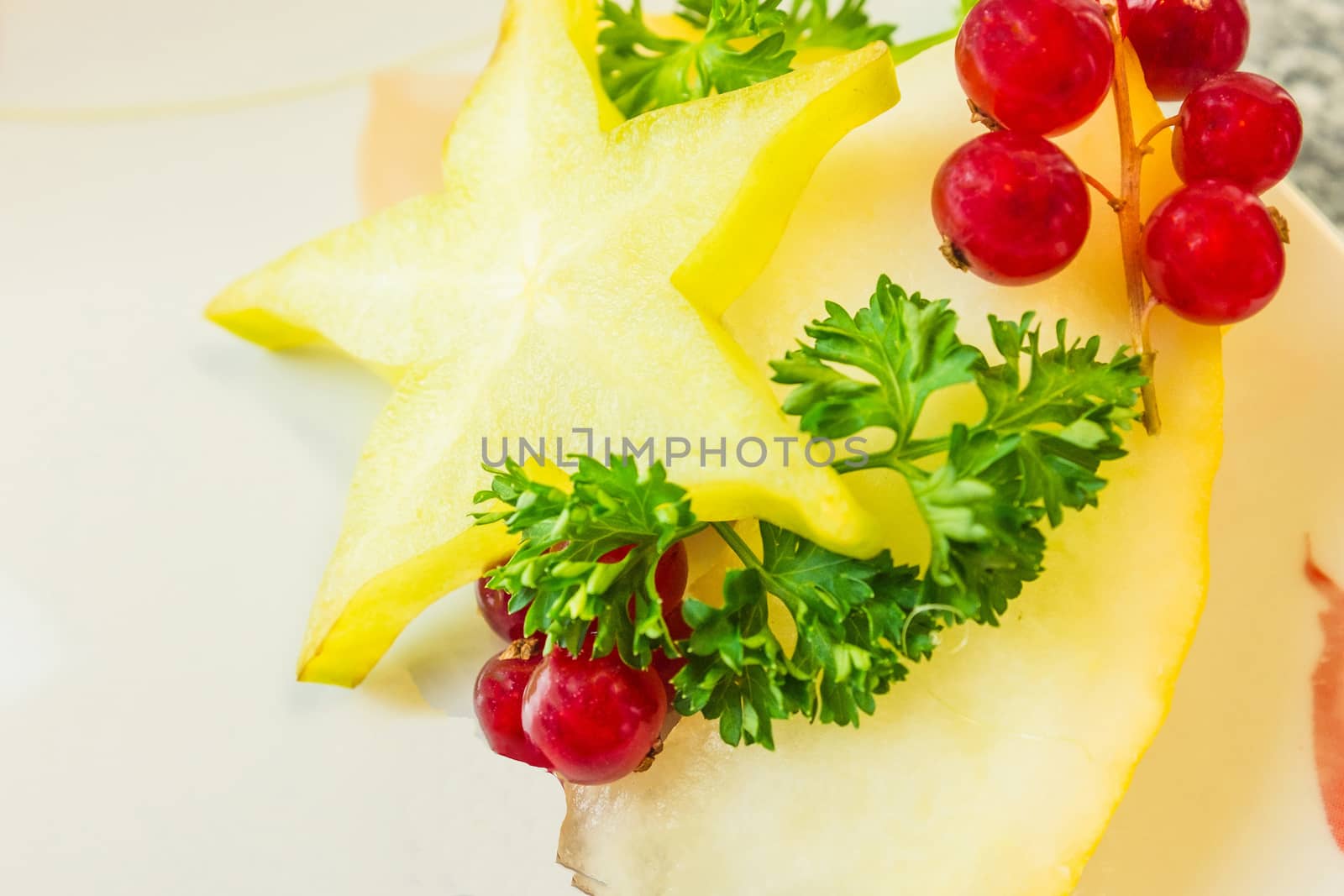 A slice of carambola or star fruit with currants with stems and parsley on a slice of melon in a white china bowl.

