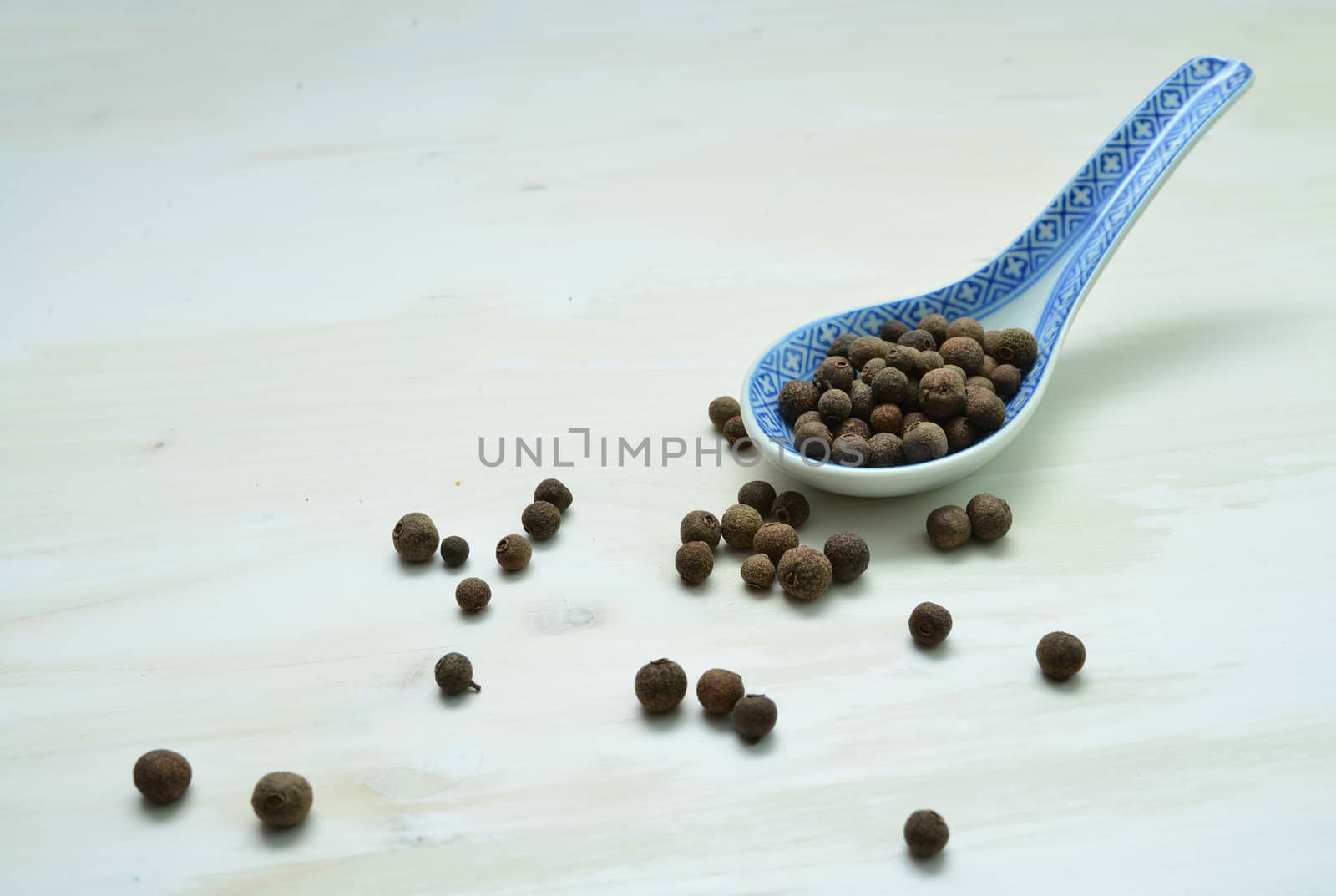 allspice seeds spoon over white wood background