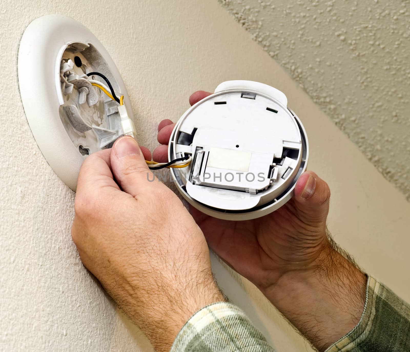 Close up hands installing smoke alarm in home.