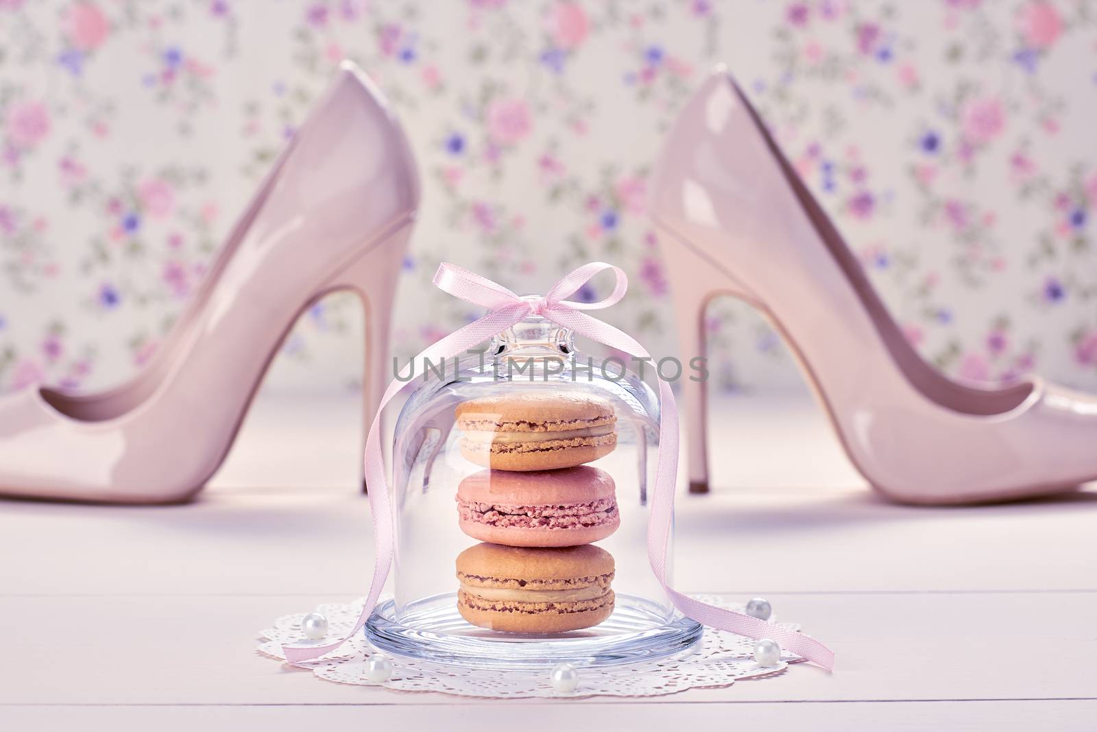 Woman essentials fashion accessories. Macarons french dessert, luxury beige shoes high heels, pearl, ribbon. Creative wedding set, vanilla wood, floral background. Romantic, still life. Retro vintage 