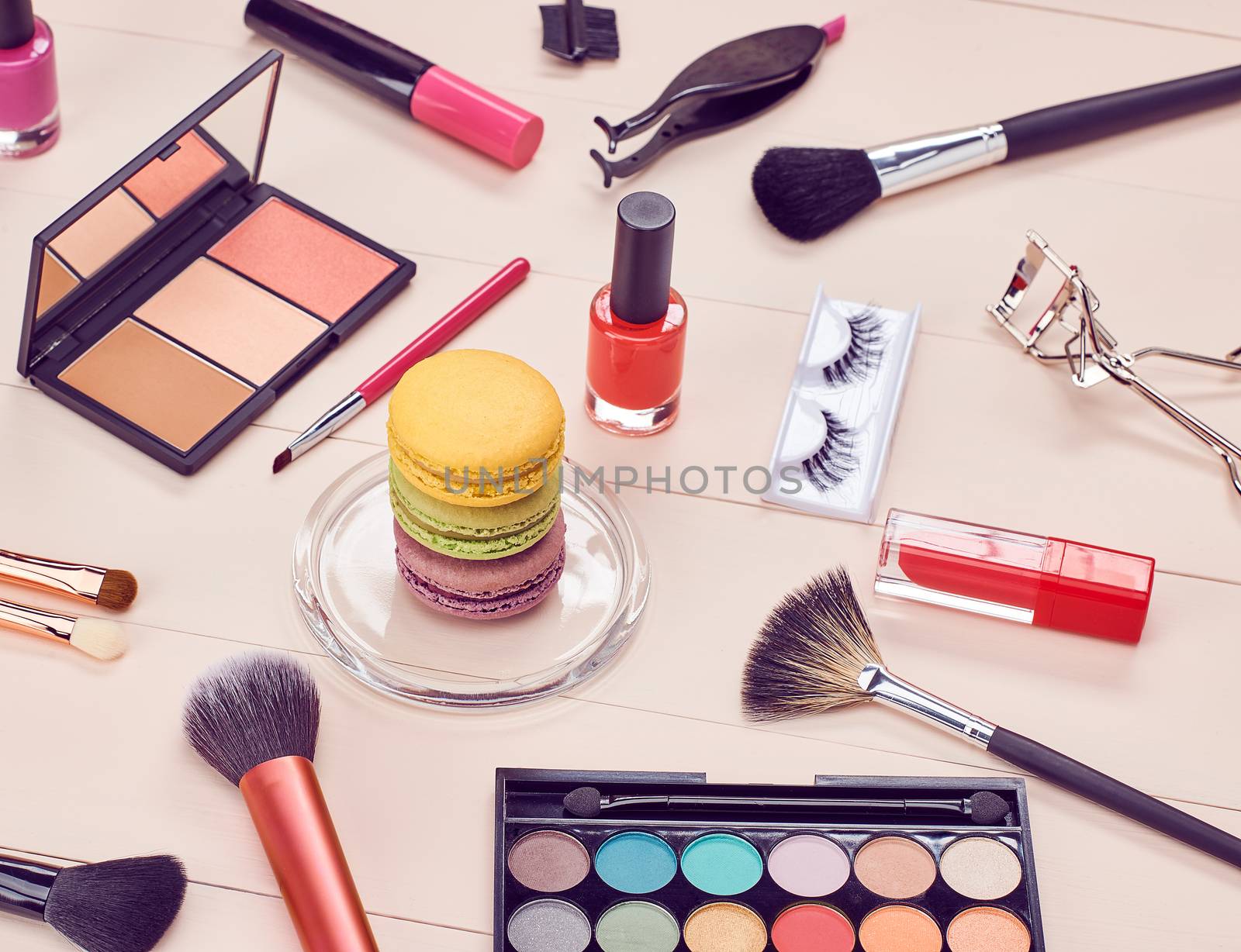 Still life, fashion woman essentials cosmetics. Beauty makeup accessories. Macarons french dessert. Lipstick, brushes, eyeshadow, false eyelashes, mascara.Unusual creative set. Vanilla wood background