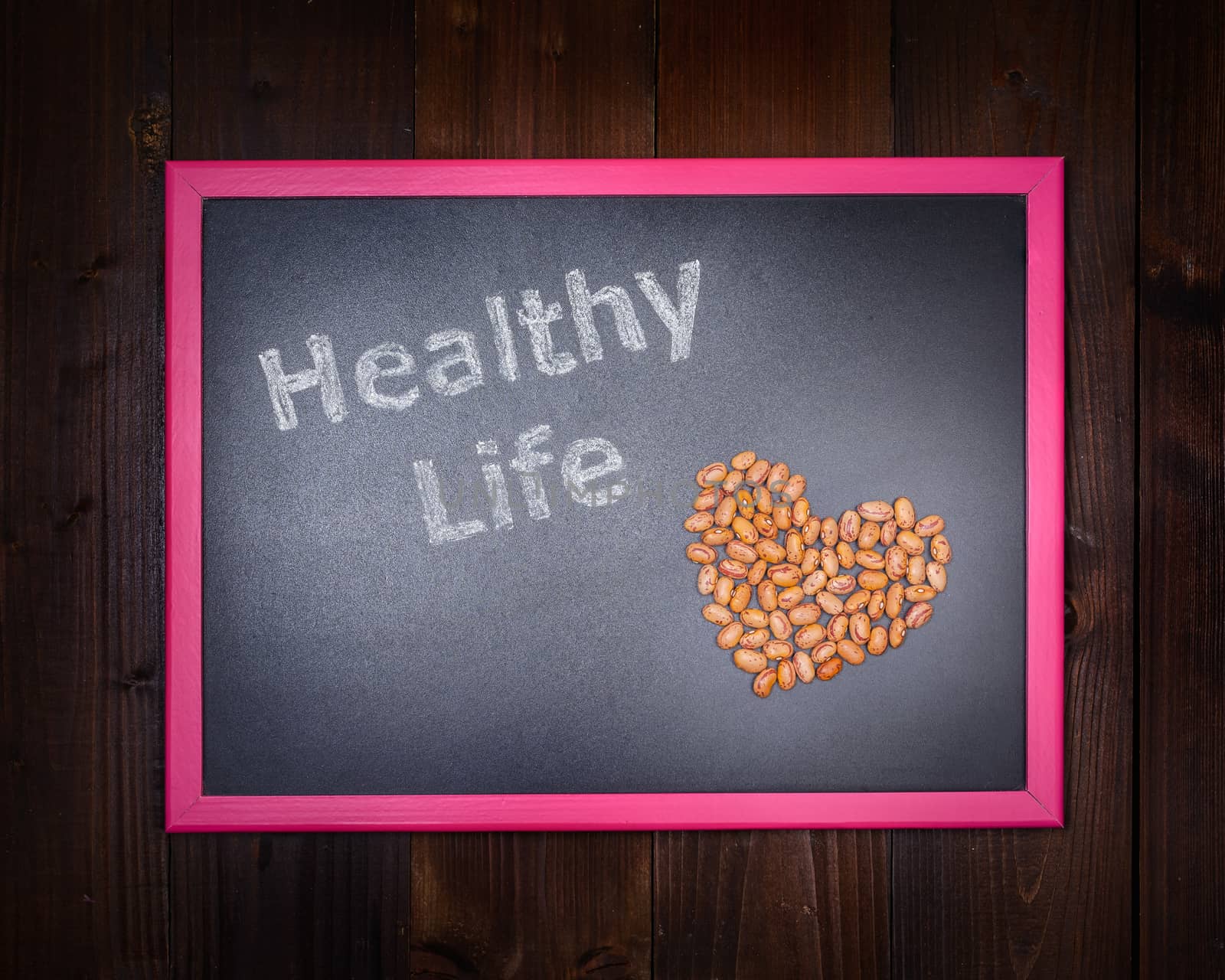 In the picture a blackboard, on the left side with written "Healthy Life" and on the right side of beans which draw a heart on wooden background