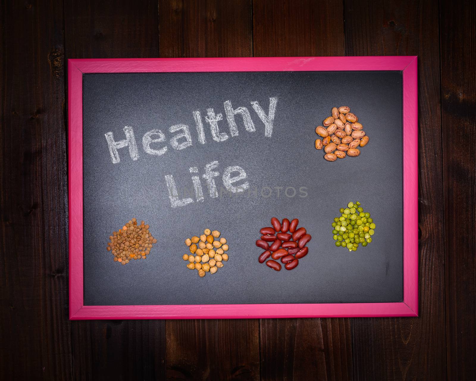 In the picture a blackboard that says "Healthy Life" and around small groups made up of chickpeas, beans, lentils and peas on wooden background